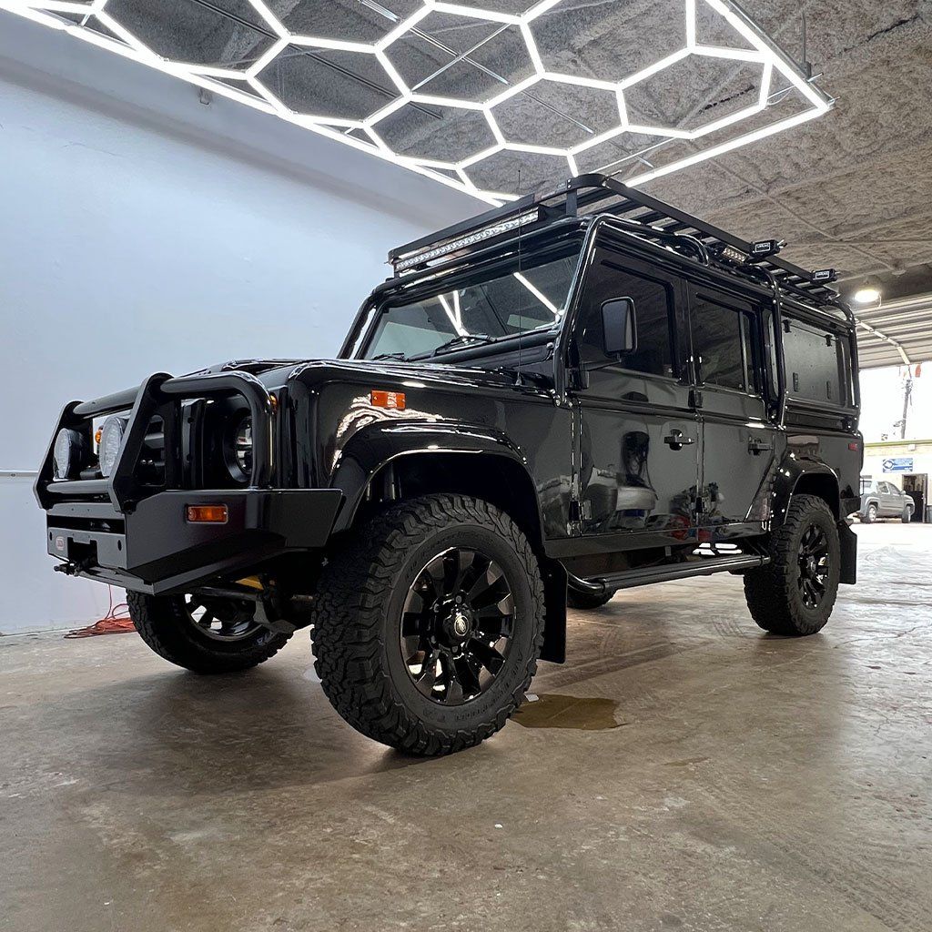 Black Land Rover Defender SUV, modified with a roof rack and off-road tires, parked indoors.
