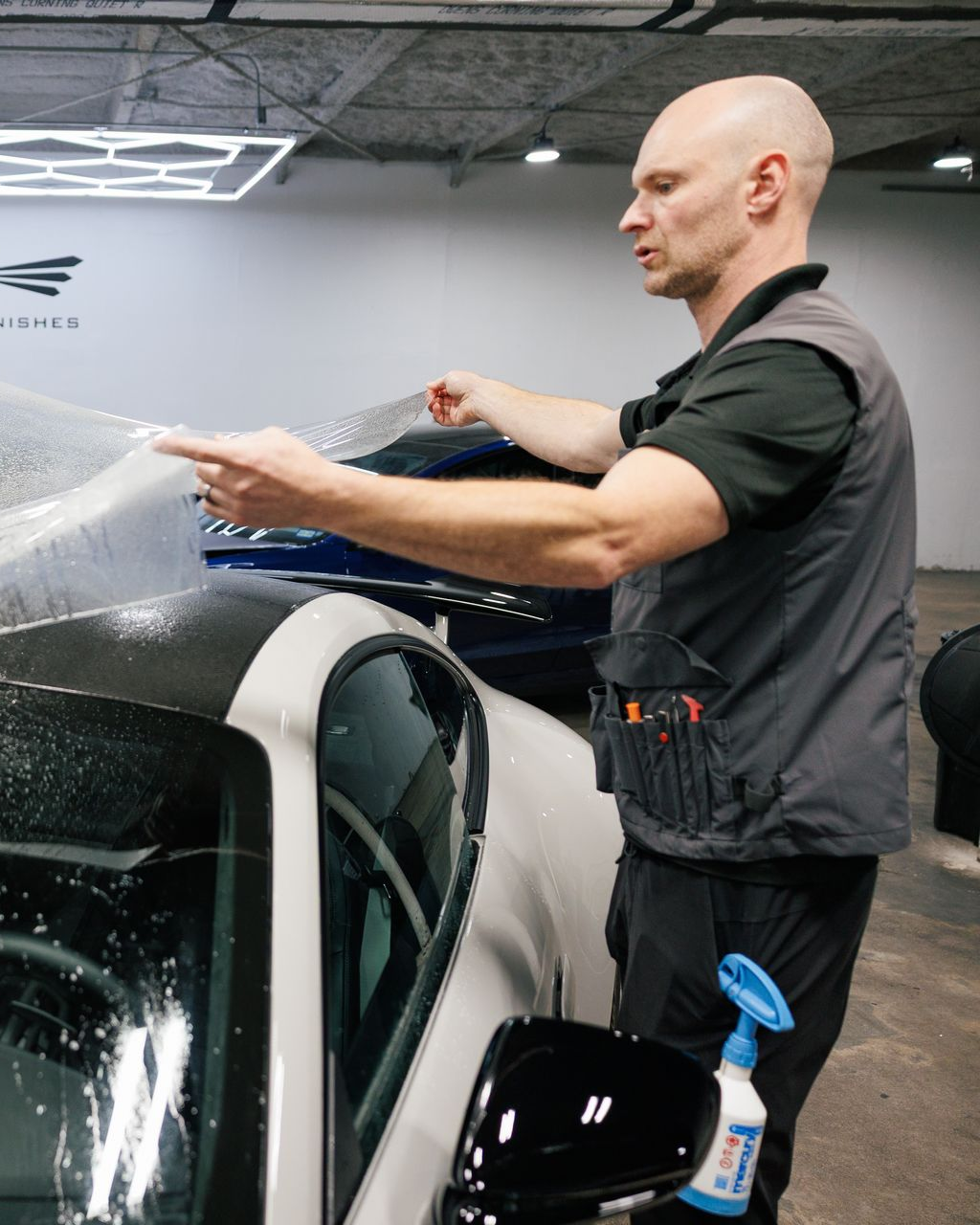 Man pointing at car while applying film in a well-lit workshop.