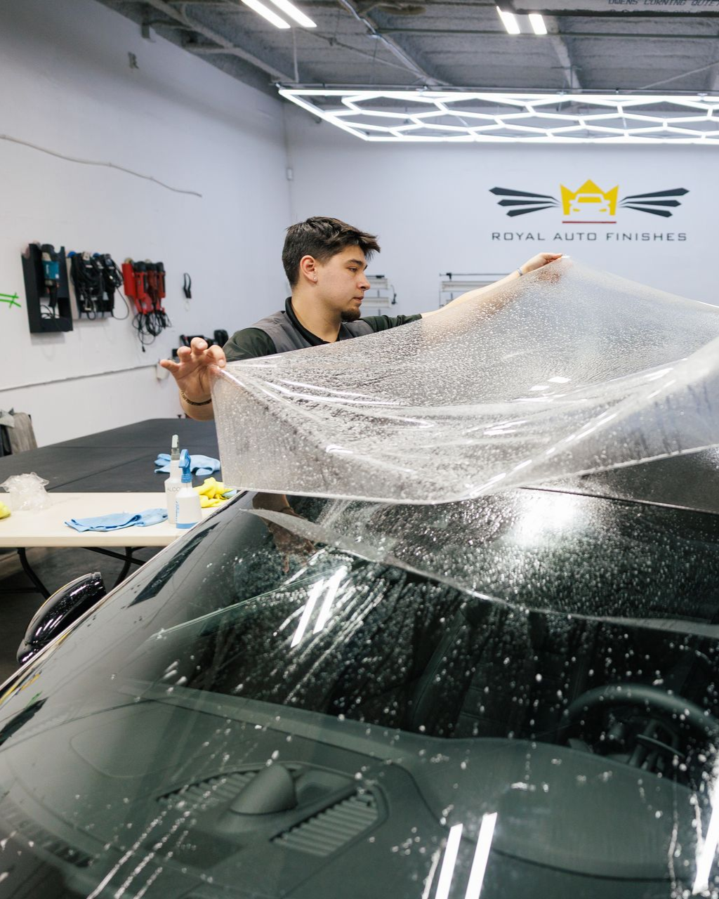 Man applying film to a car windshield in an auto shop.