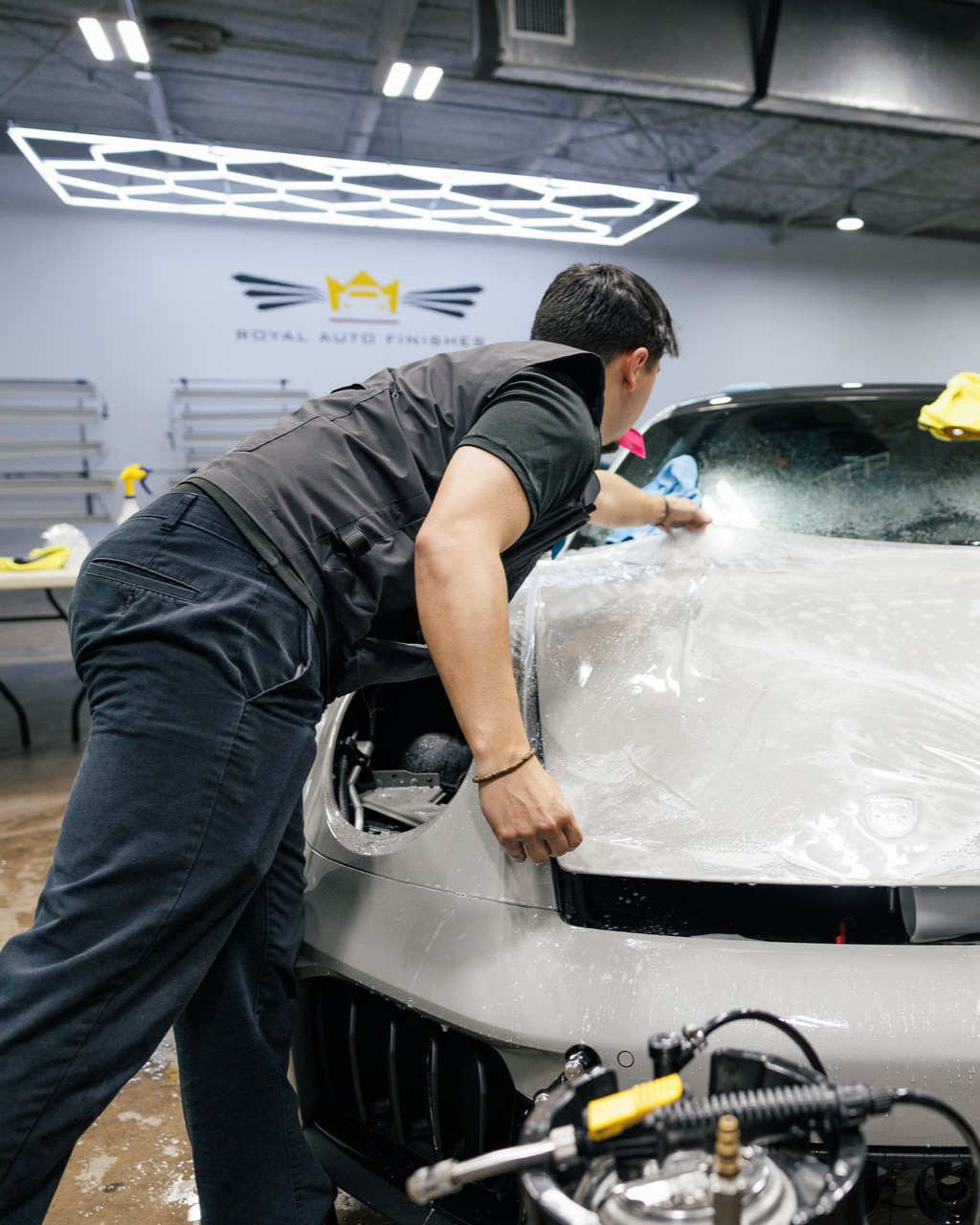 Person applying protective film to a car's hood in a shop.