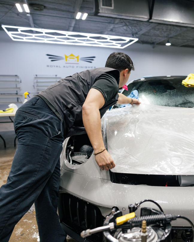 Person applying protective film to a car's hood in a shop.