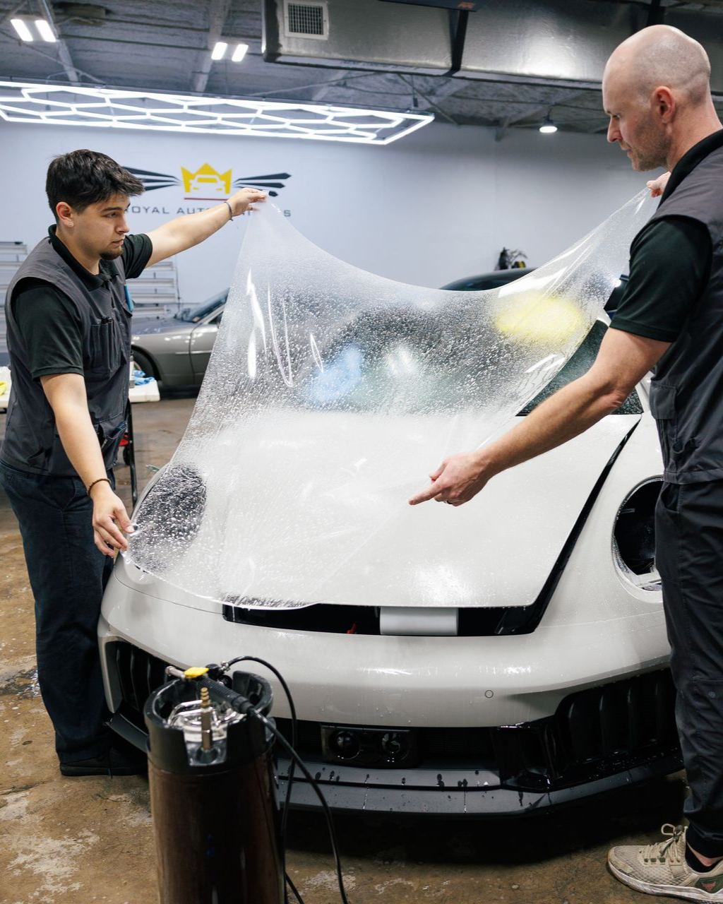 Man holding large clear film in front of a car in a garage.