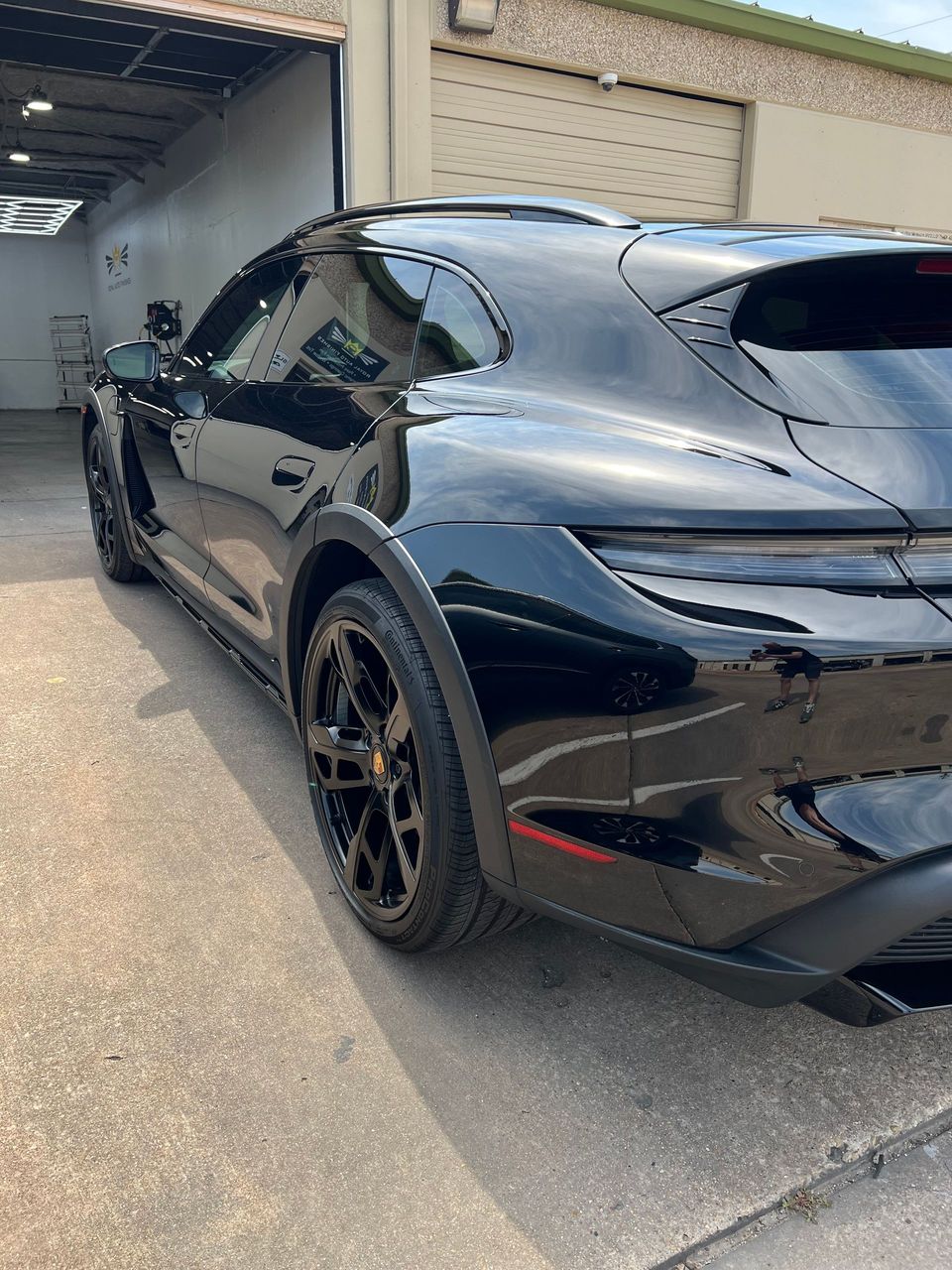 Black Porsche coupe parked under a car wash bay.