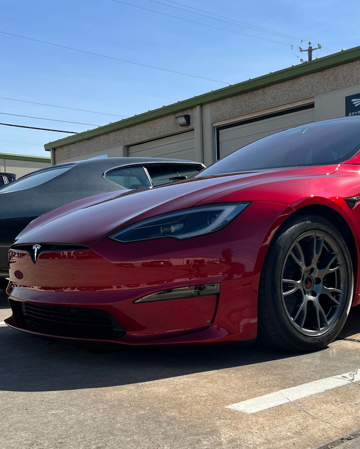 Red Tesla sedan parked outside a building with tinted windows.