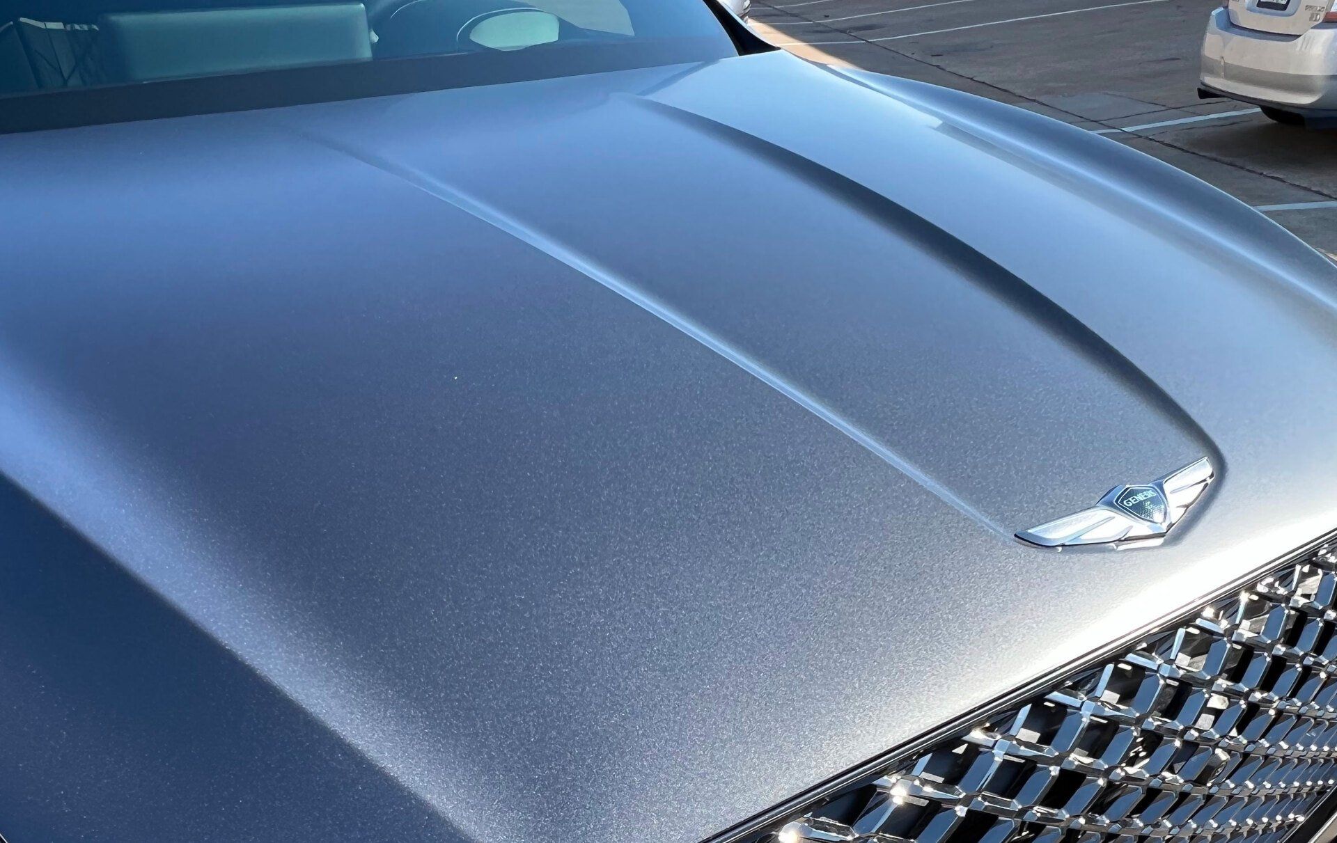 Close-up of a silver car hood with a centered emblem and a shiny, textured surface.