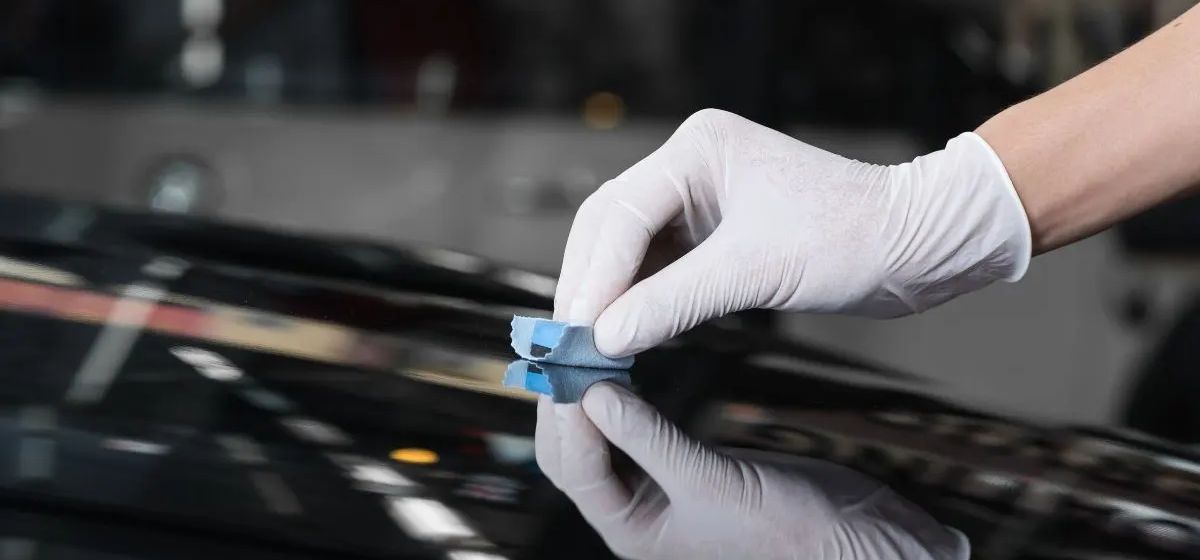 Gloved hand applying a blue pad to a shiny, black surface, likely a car.