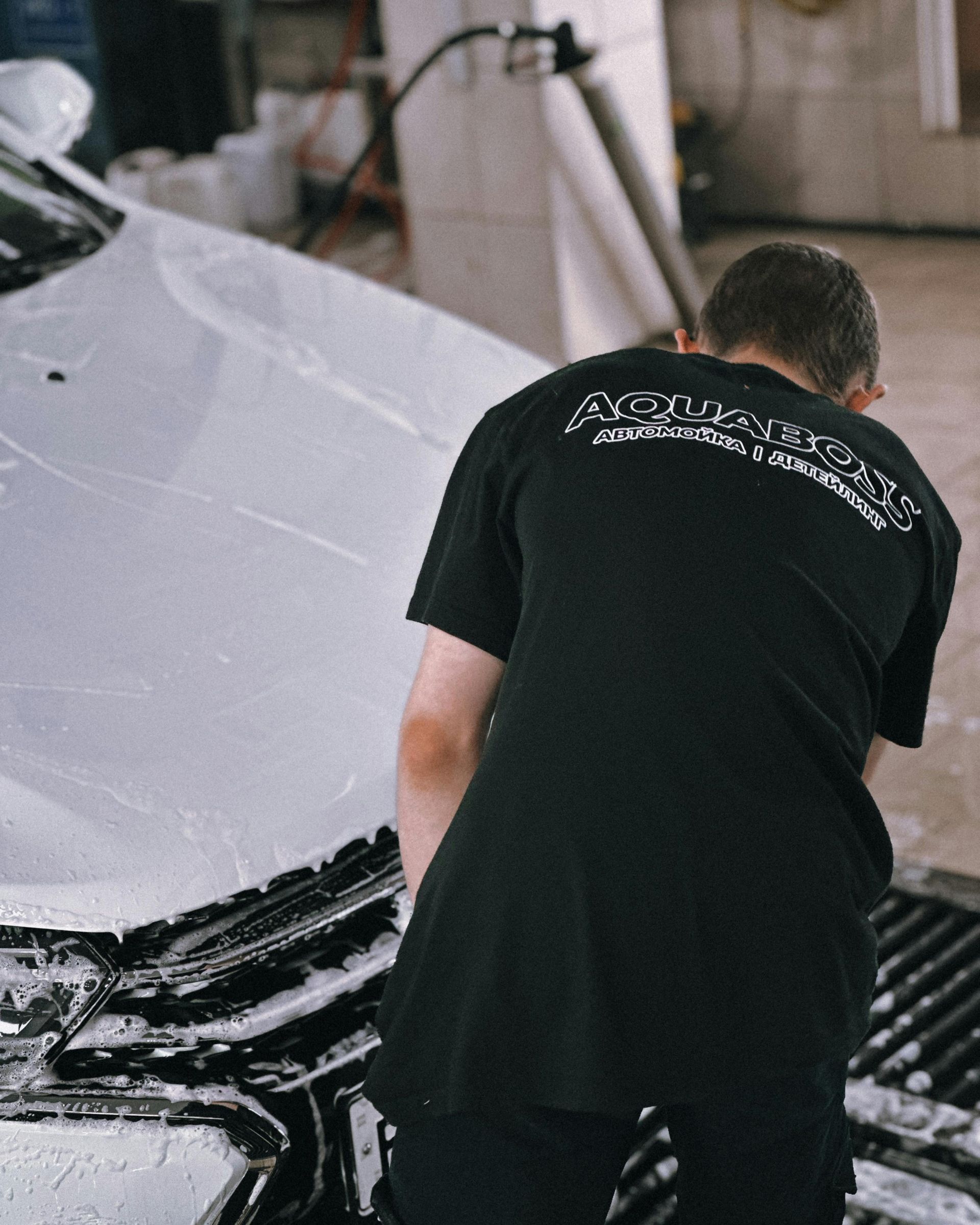 Man washes a white car, covered in foam, in a car wash.