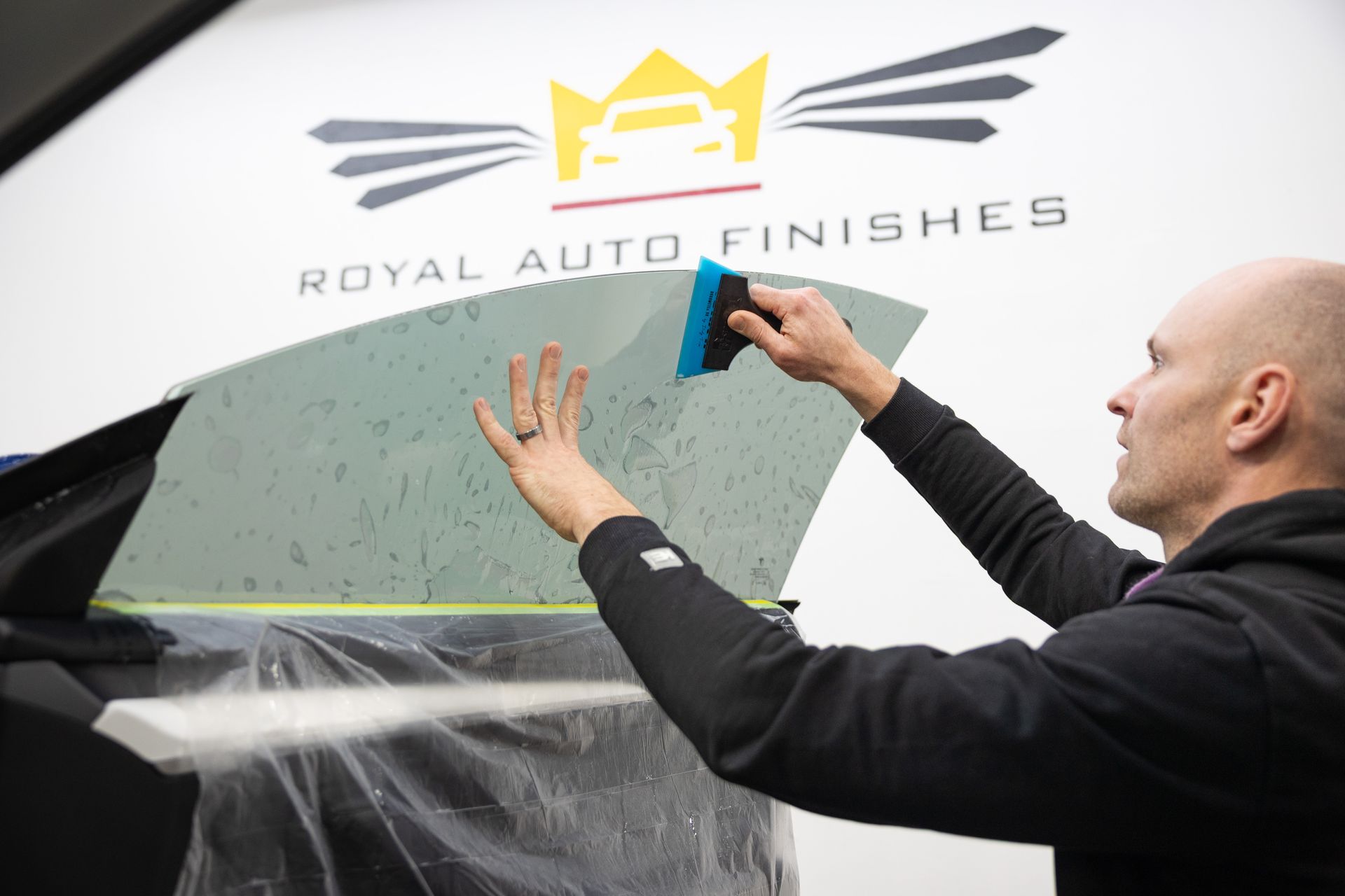 Man applying window tint to a car window at Royal Auto Finishes.
