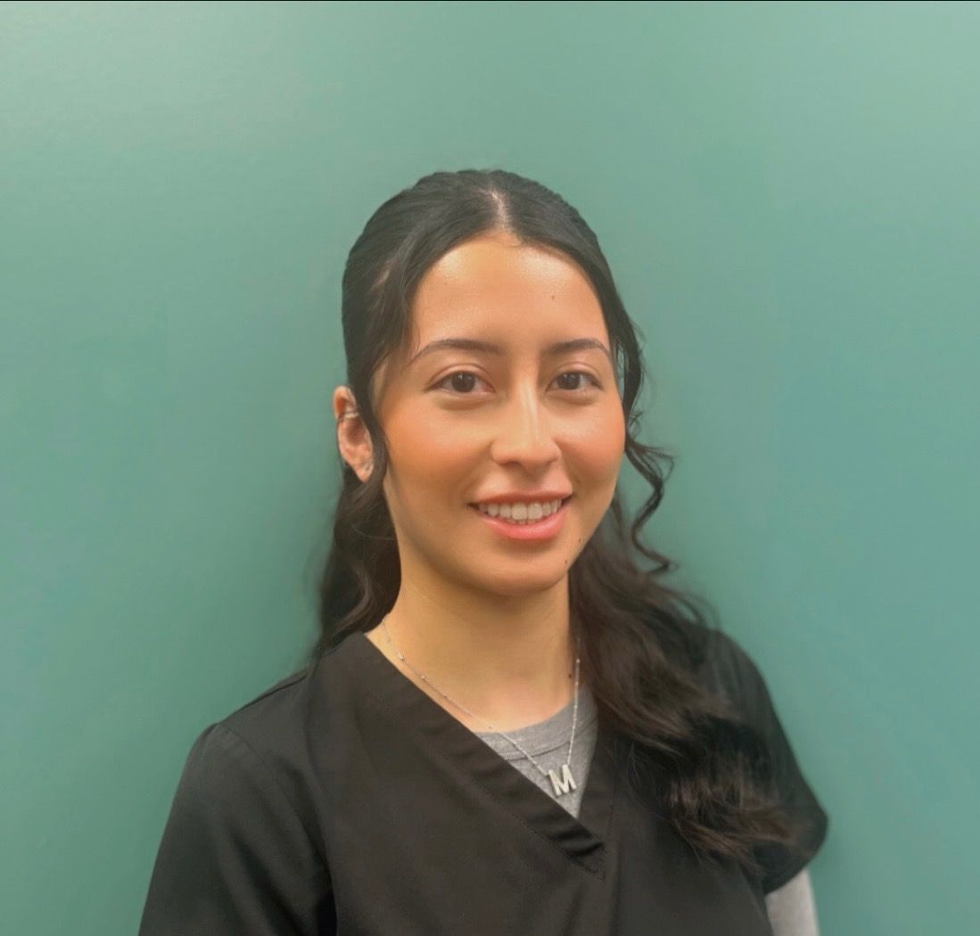 A woman in a black scrub top is smiling in front of a green wall.