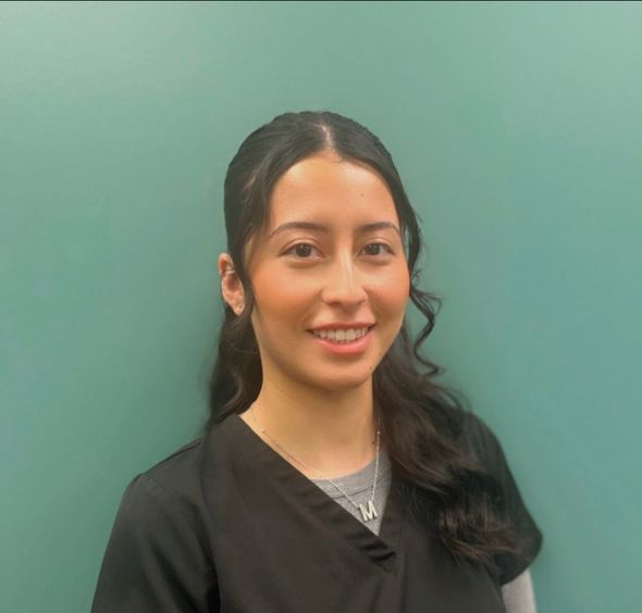 A woman in a black scrub top is smiling in front of a green wall.