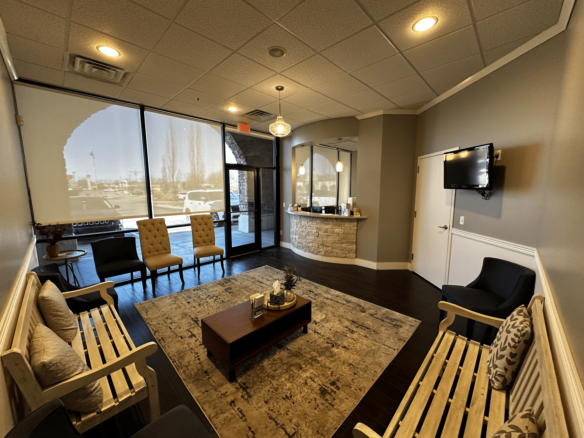 A waiting room with a couch , chairs , coffee table and television.