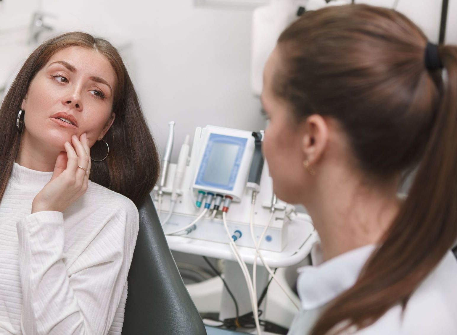 A woman is sitting in a dental chair looking at her face in the mirror.