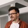 A man wearing glasses and a red shirt is smiling