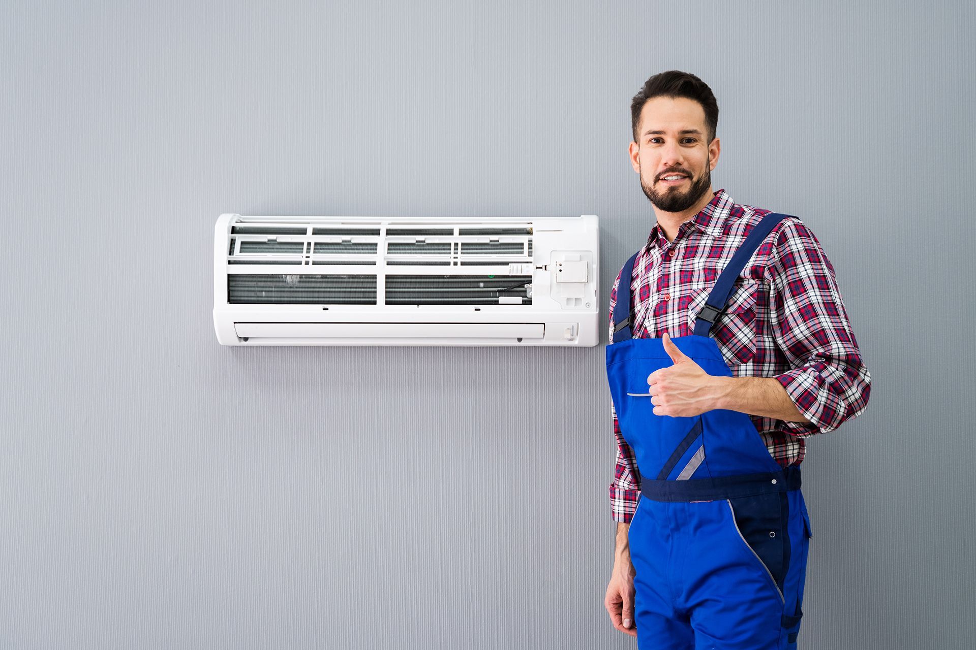 A man is standing in front of an air conditioner and giving a thumbs up.