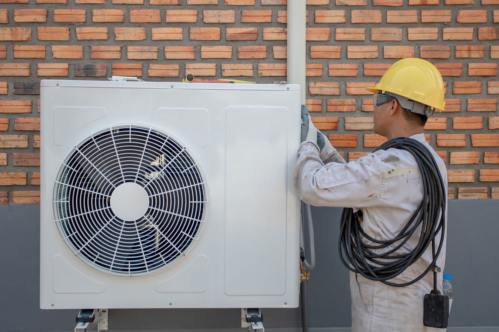 A man is installing an air conditioner on a brick wall.