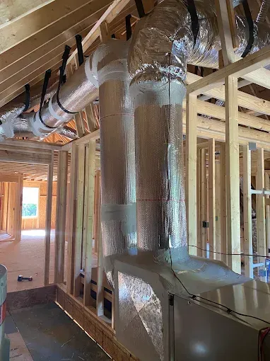 Interior wall framing with insulated HVAC ducts and vents in an unfinished house under construction