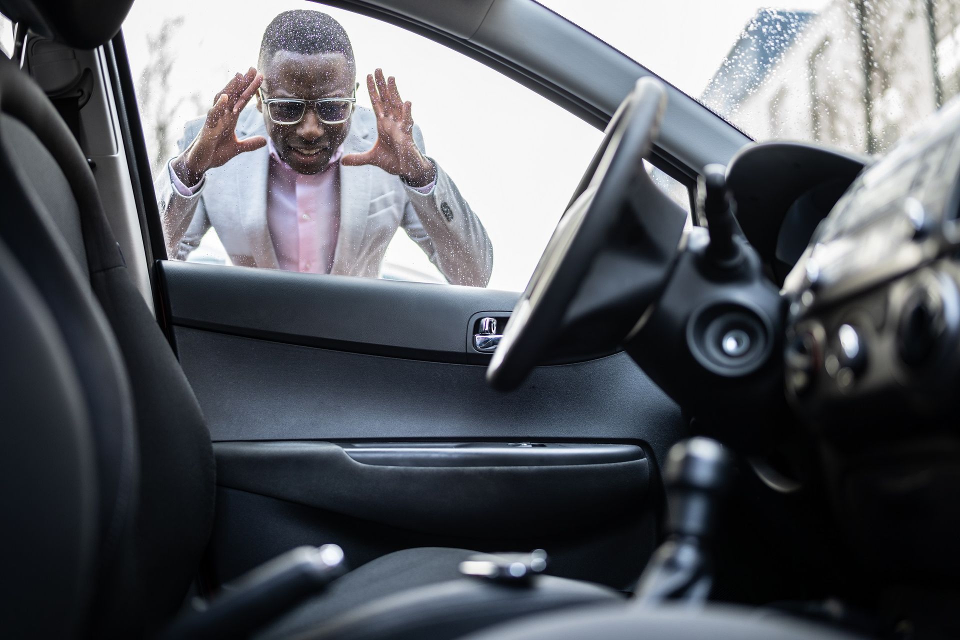 Man locked out of a car, hands raised in distress. Interior car view, focus on the open door.