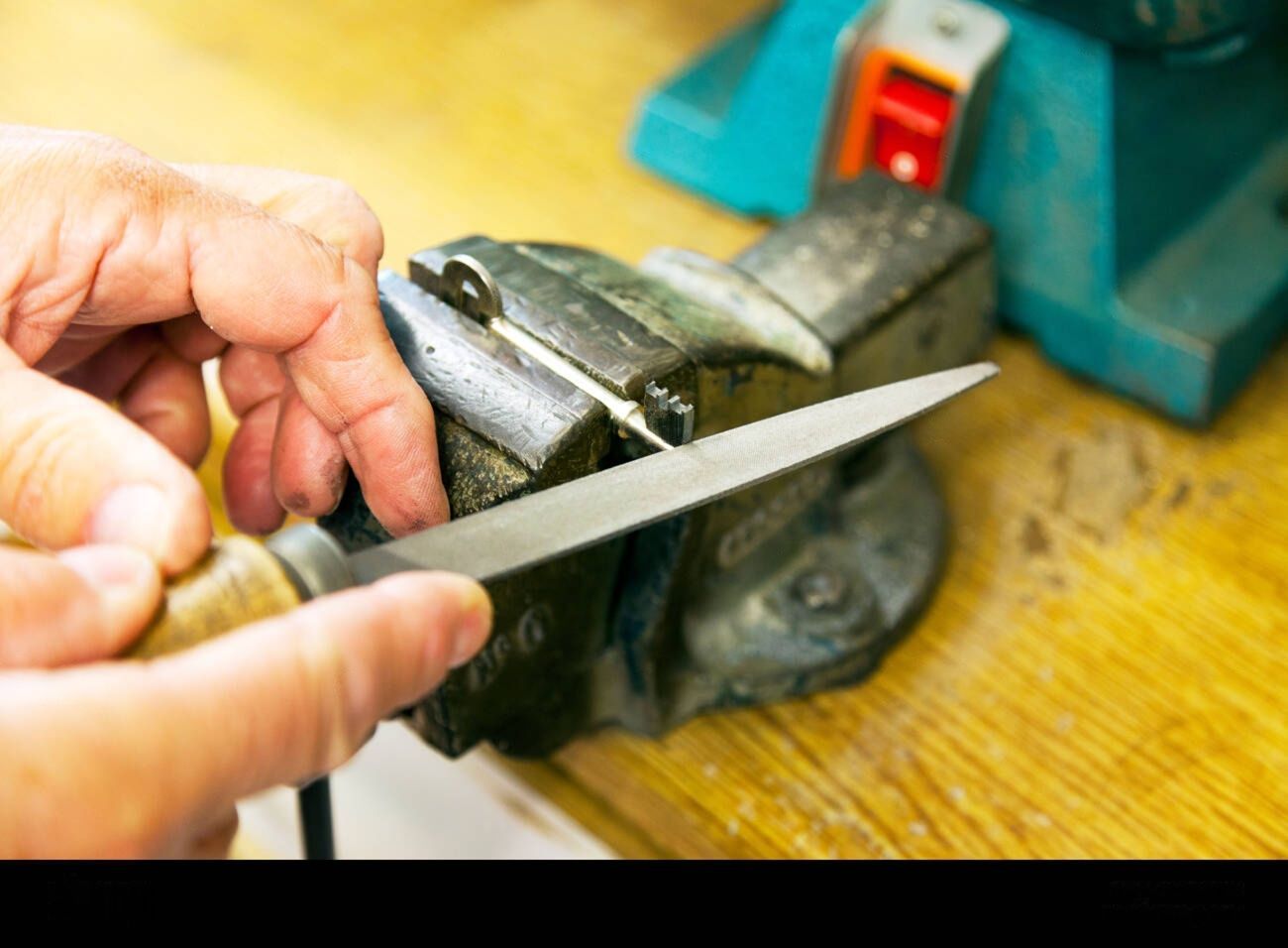 Hand filing metal held in a vise. Wooden workbench.