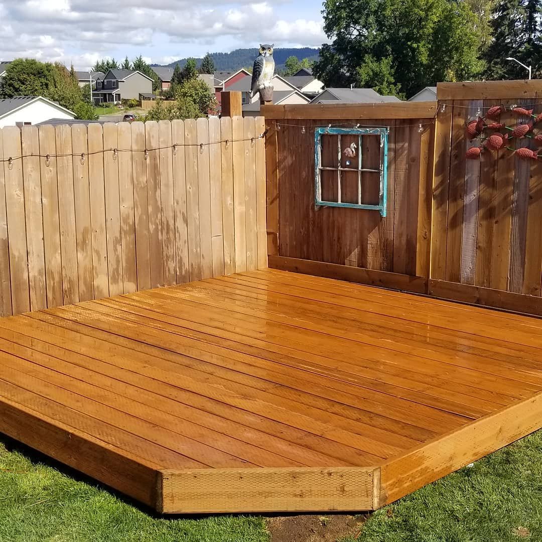 Wooden deck with fence, small window, and green grass. Sunlight and brown tones.
