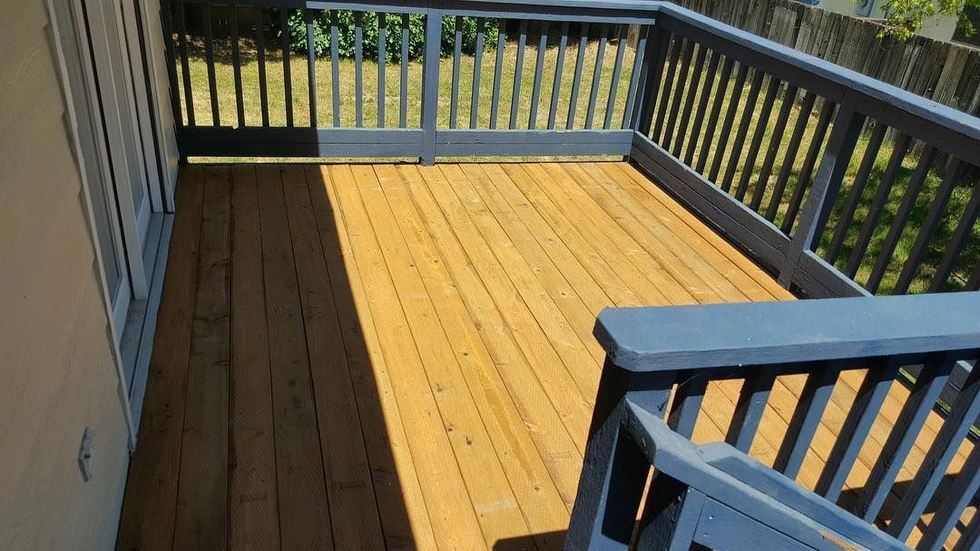 Wooden deck with blue railings, next to a beige wall. 