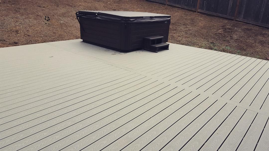 Hot tub on a light-colored, slatted deck in an outdoor setting with brown grass and a wooden fence.