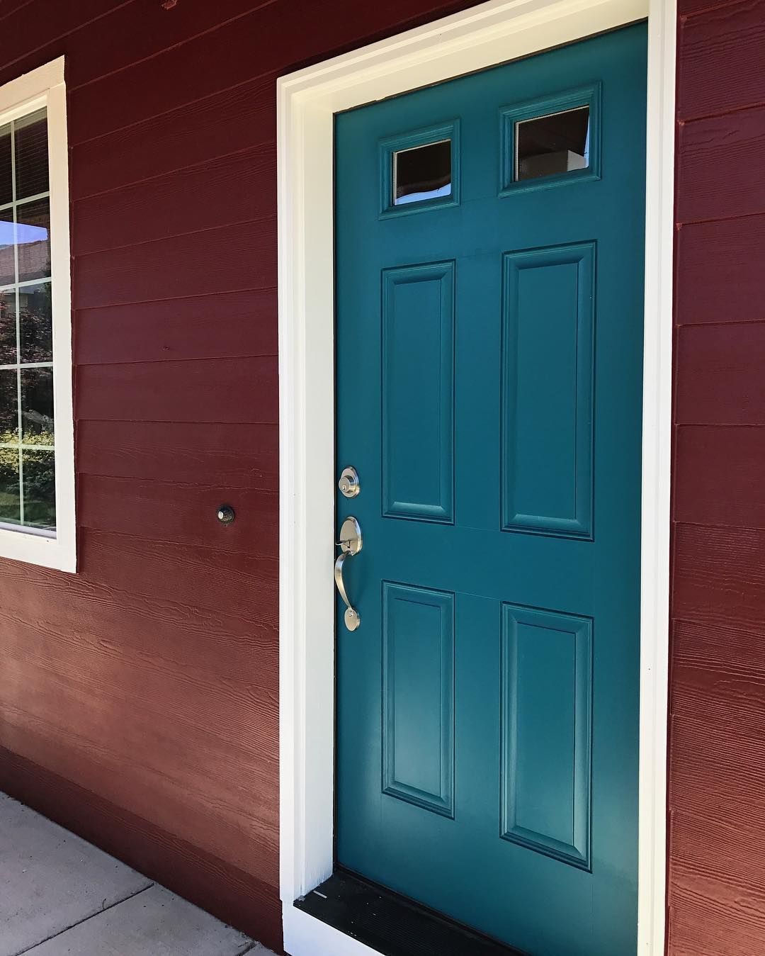 Teal front door with white trim, red siding, and a small window.