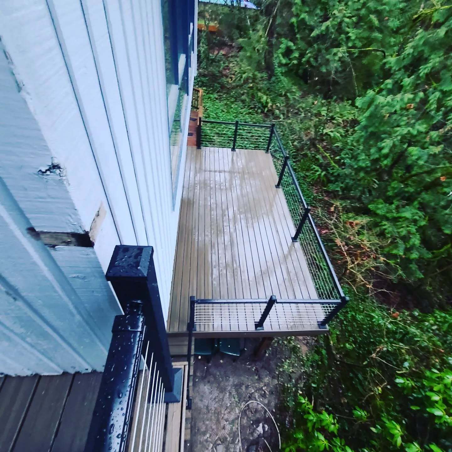 Wooden deck attached to a white building with black railings overlooking a green forest.