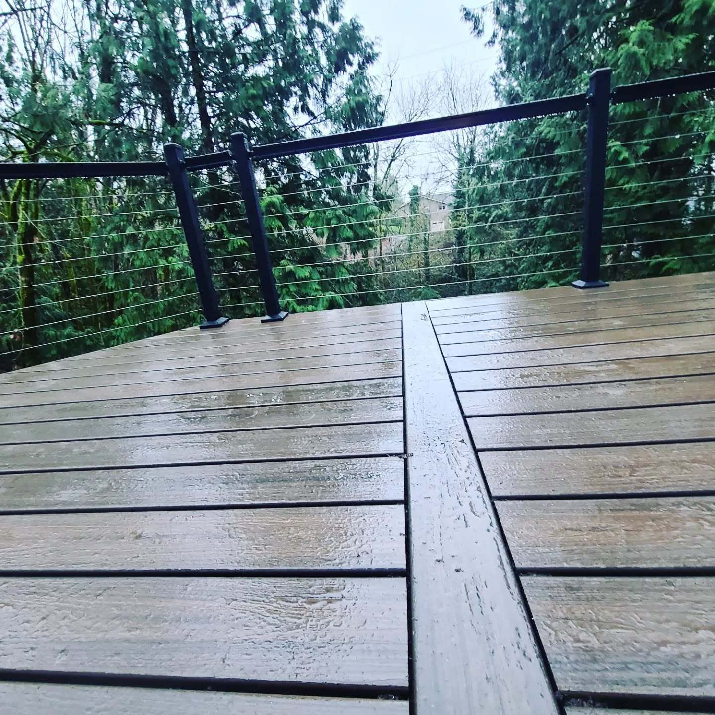 Wet composite deck with a metal railing and trees in the background.