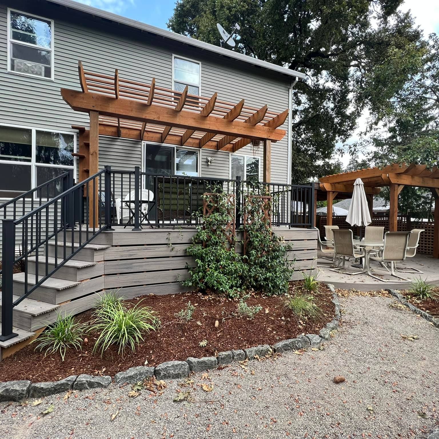 Wooden pergola over a deck with black railing and steps leading to a gravel patio.