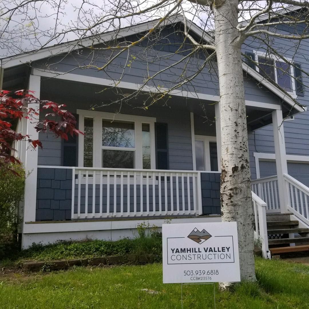 House for auction, light blue siding, white porch, sign on lawn, tree in front.