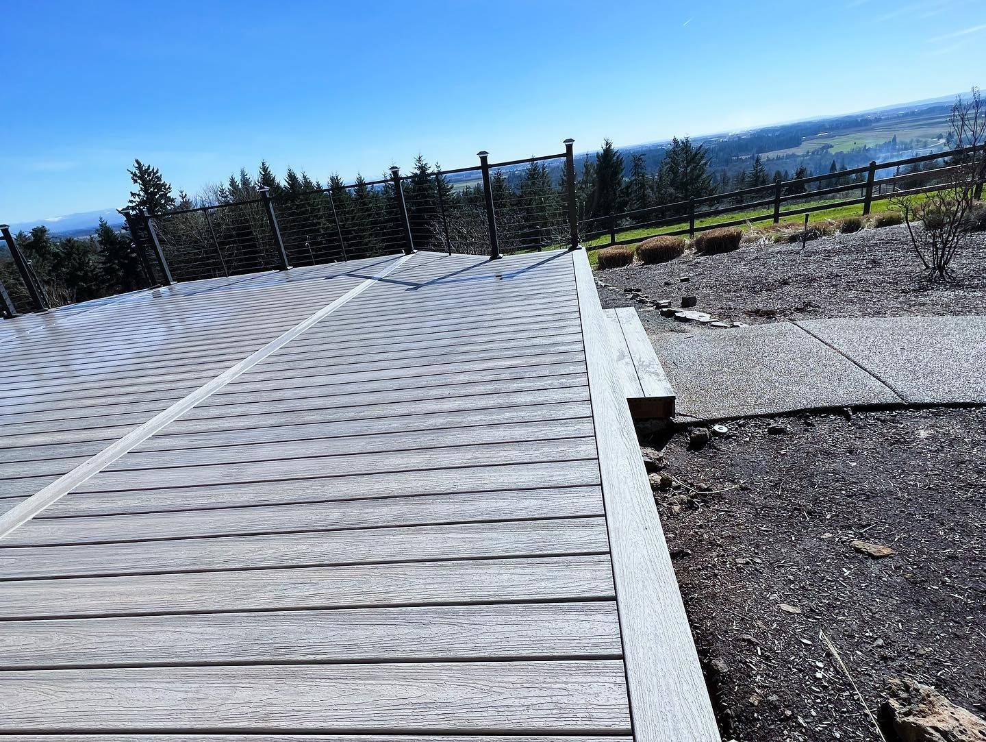 Wooden walkway with safety cable, overlooking a landscape with trees under a blue sky.