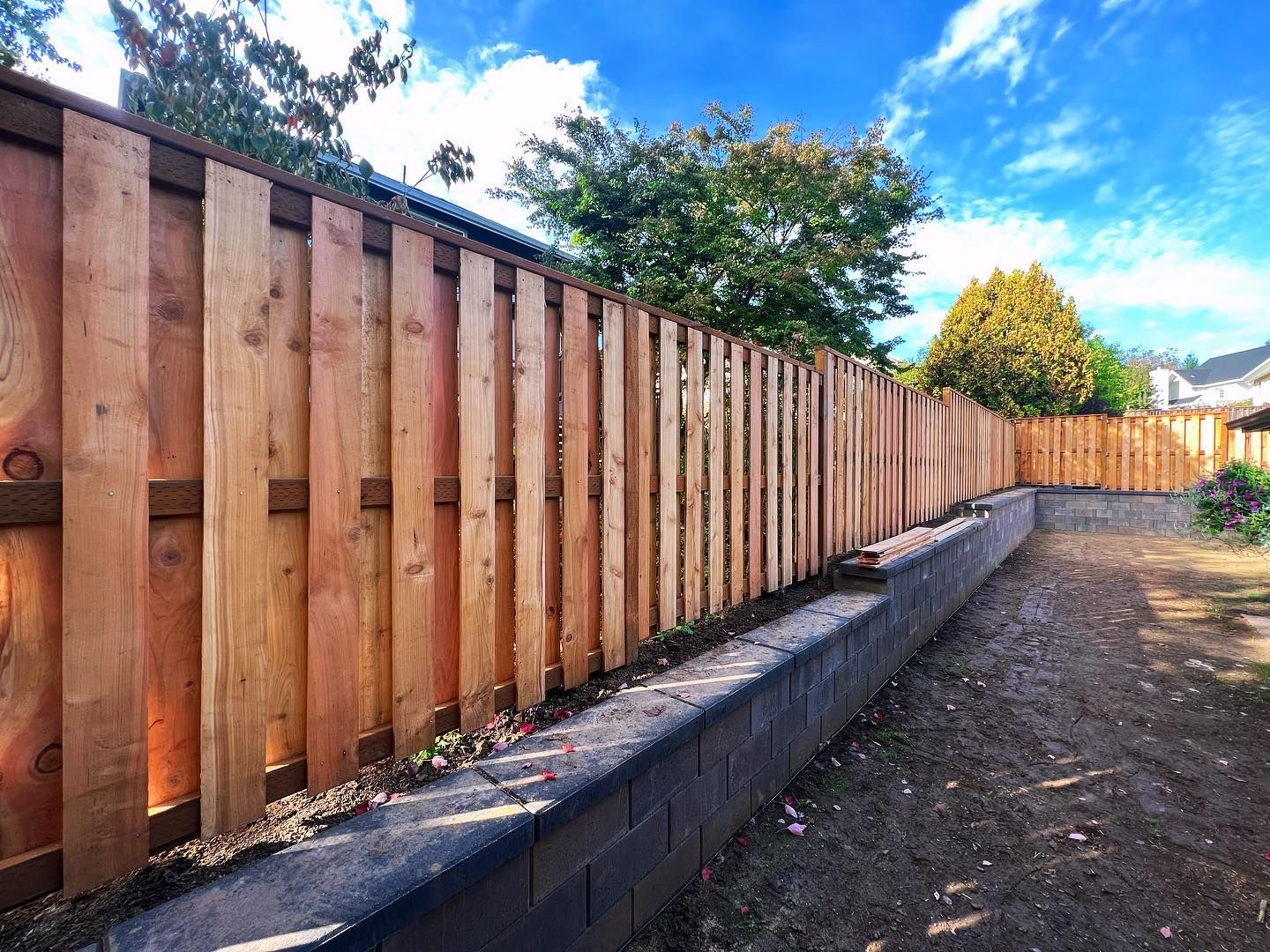 Wooden fence with vertical planks atop a concrete retaining wal.
