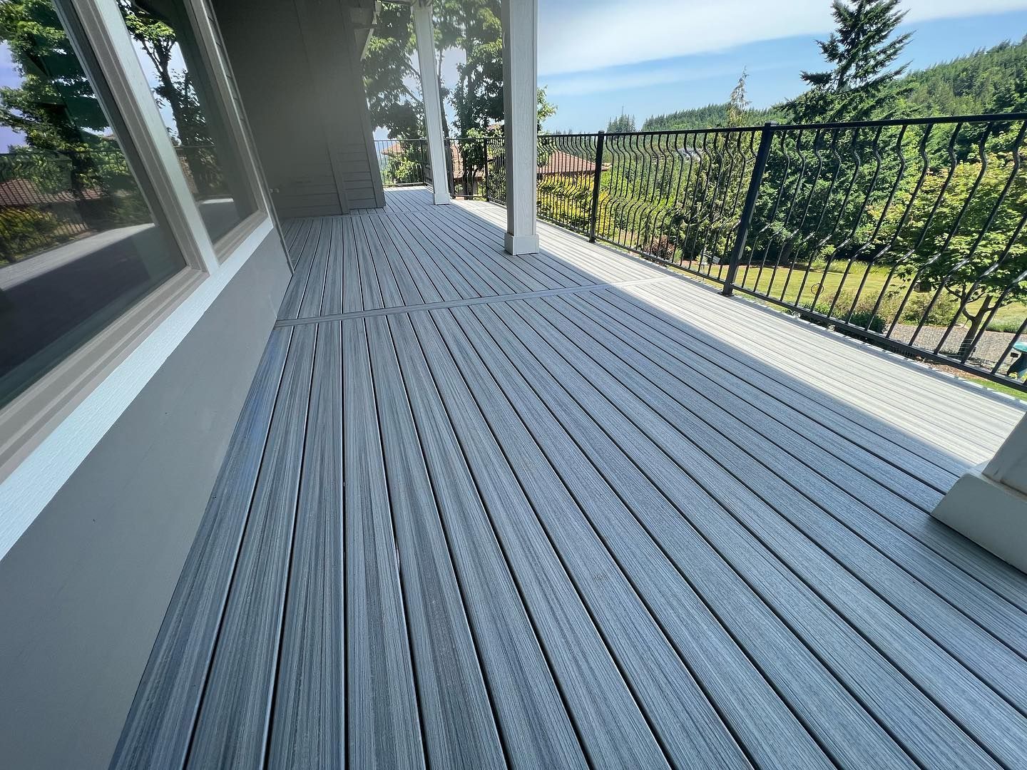 Gray composite deck with a black railing, overlooking trees and a distant body of water.