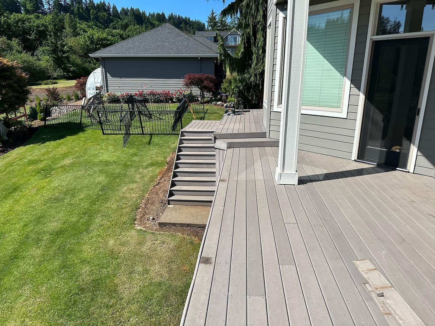 Gray deck with steps down to a green lawn, house in the background on a sunny day.