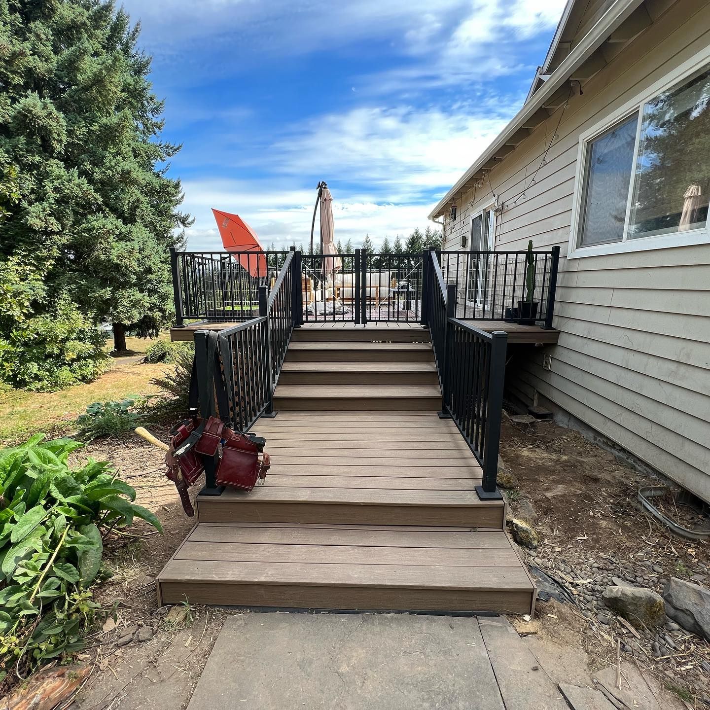 Wooden deck with steps, black railing, attached to a house with a blue sky background.