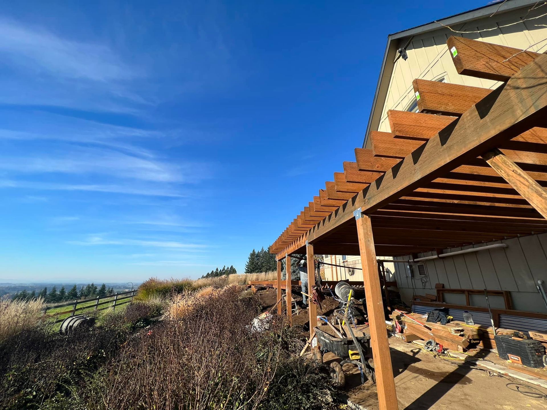Pergola extending from a house, overlooking a landscape under a blue sky.