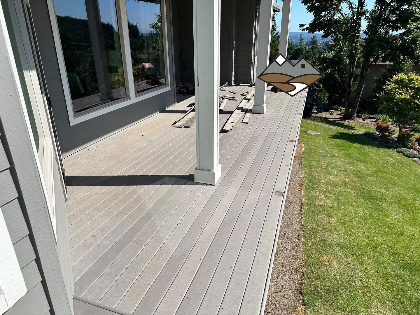 Gray composite deck with white columns, adjacent to grass and a windowed wall.