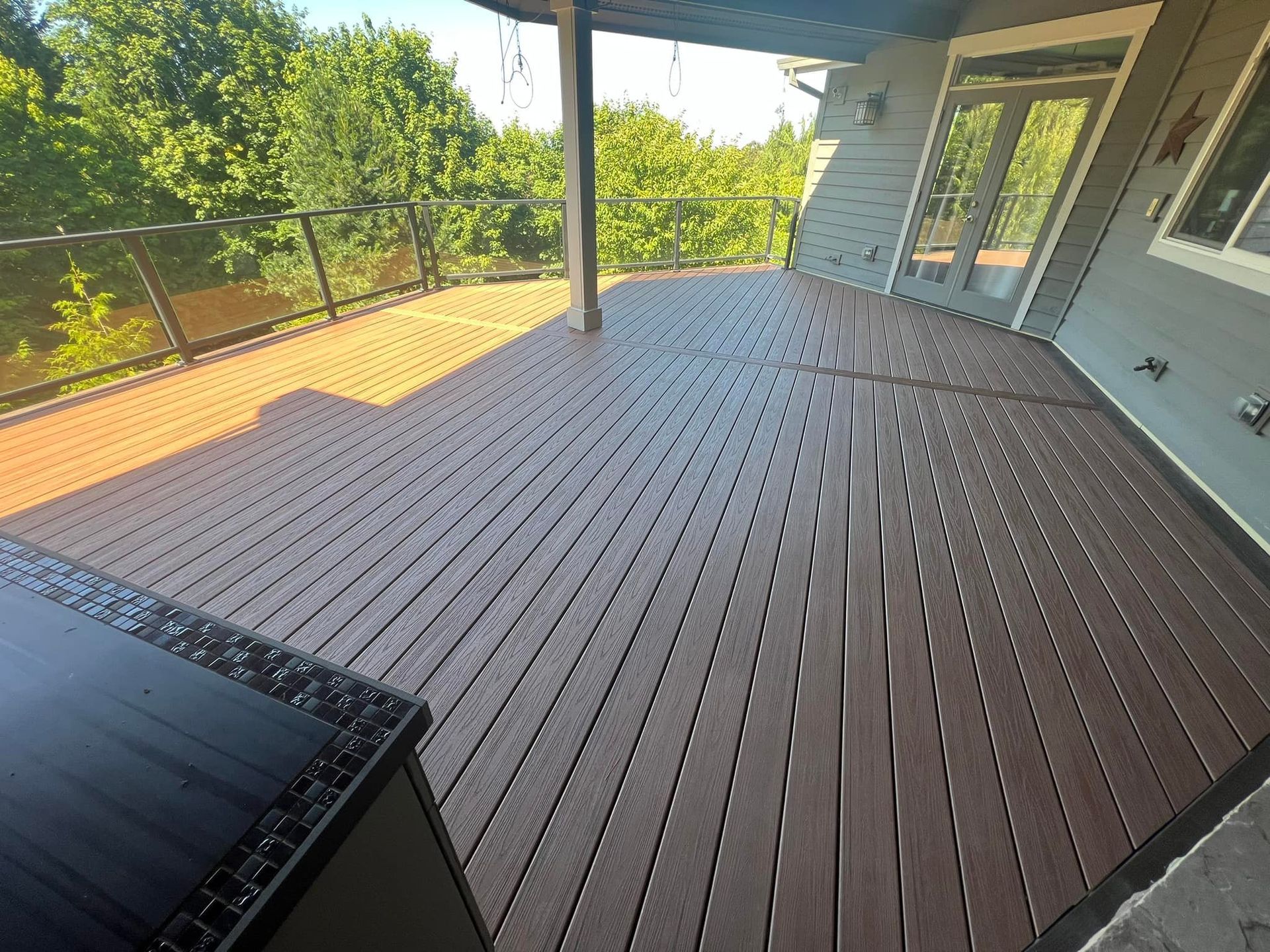 Wooden deck with brown planks. Exterior of a house with trees in the background.
