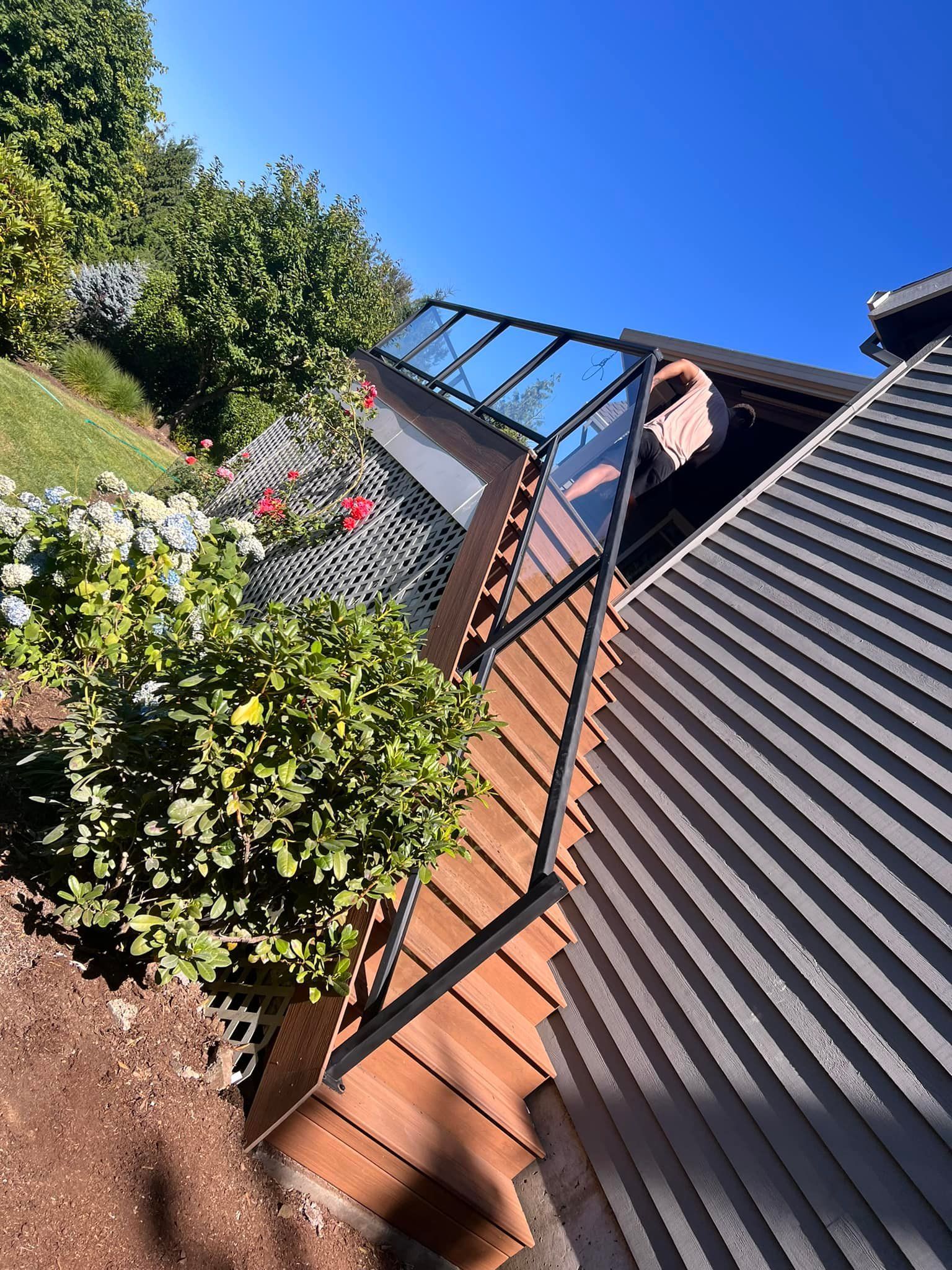 A deck with a glass railing next to a sloped garden under a clear, blue sky.