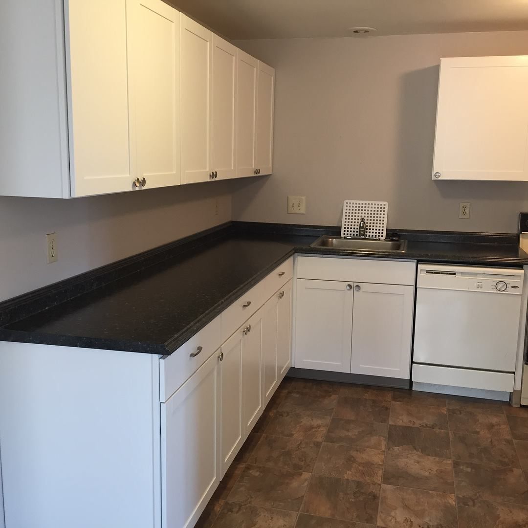 White kitchen cabinets and appliances with a dark countertop and brown flooring.