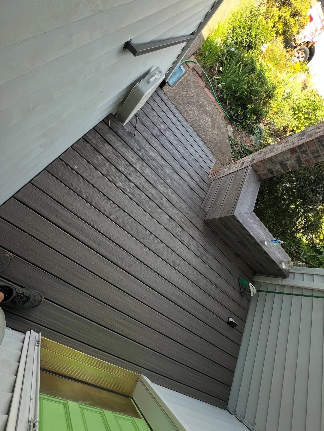 Composite deck with brick trim next to a building, sunlight, and a car.