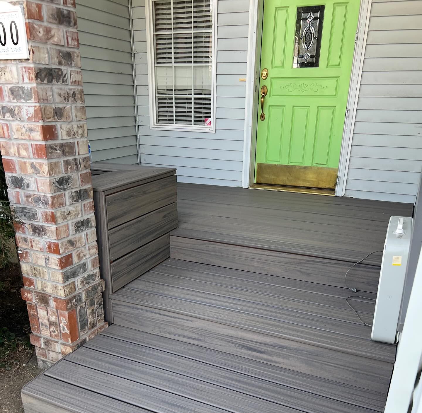 Gray composite deck with steps, a green door, and brick pillar.