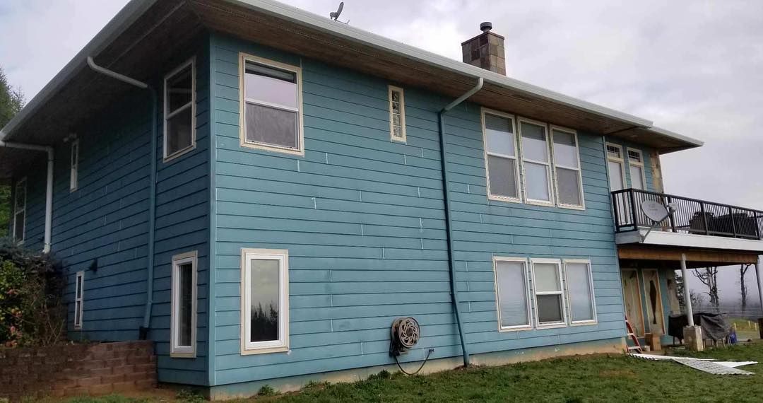Blue two-story house with white-framed windows, gutters, and a chimney on a grassy plot.