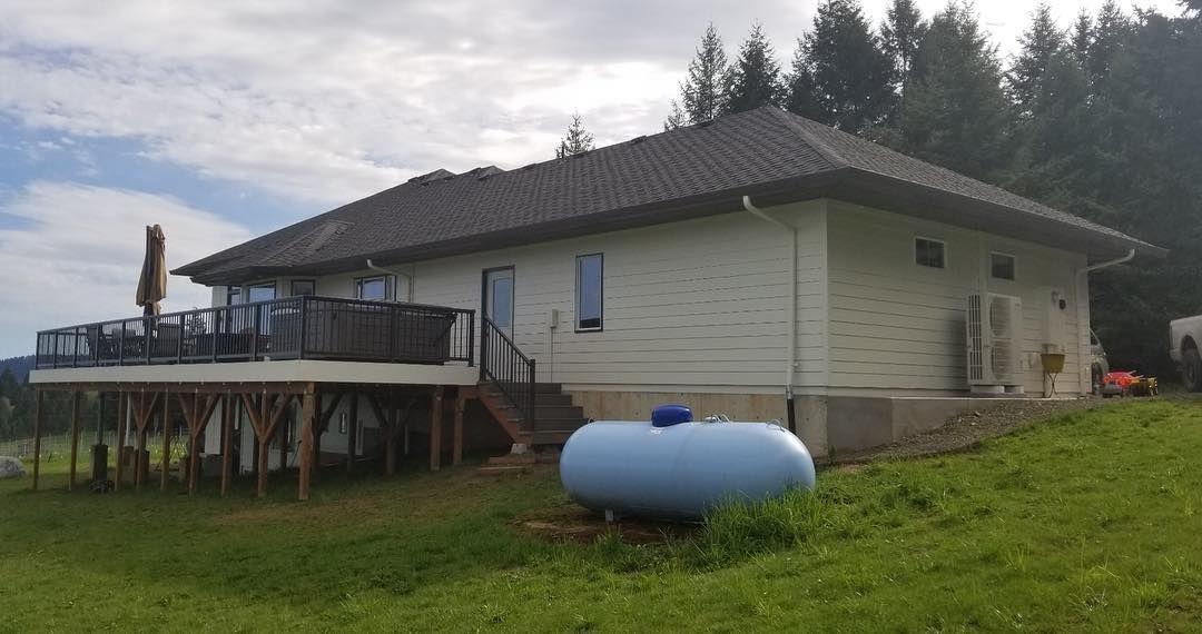 White house with a deck, propane tank in yard, and green grass.