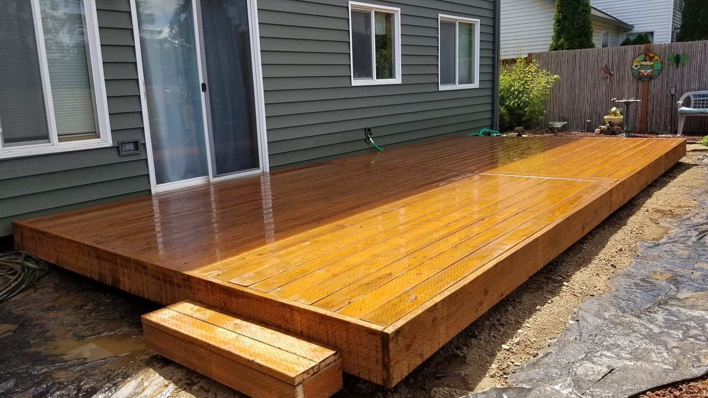 Wooden deck with two steps next to a house with a sliding glass door and windows.