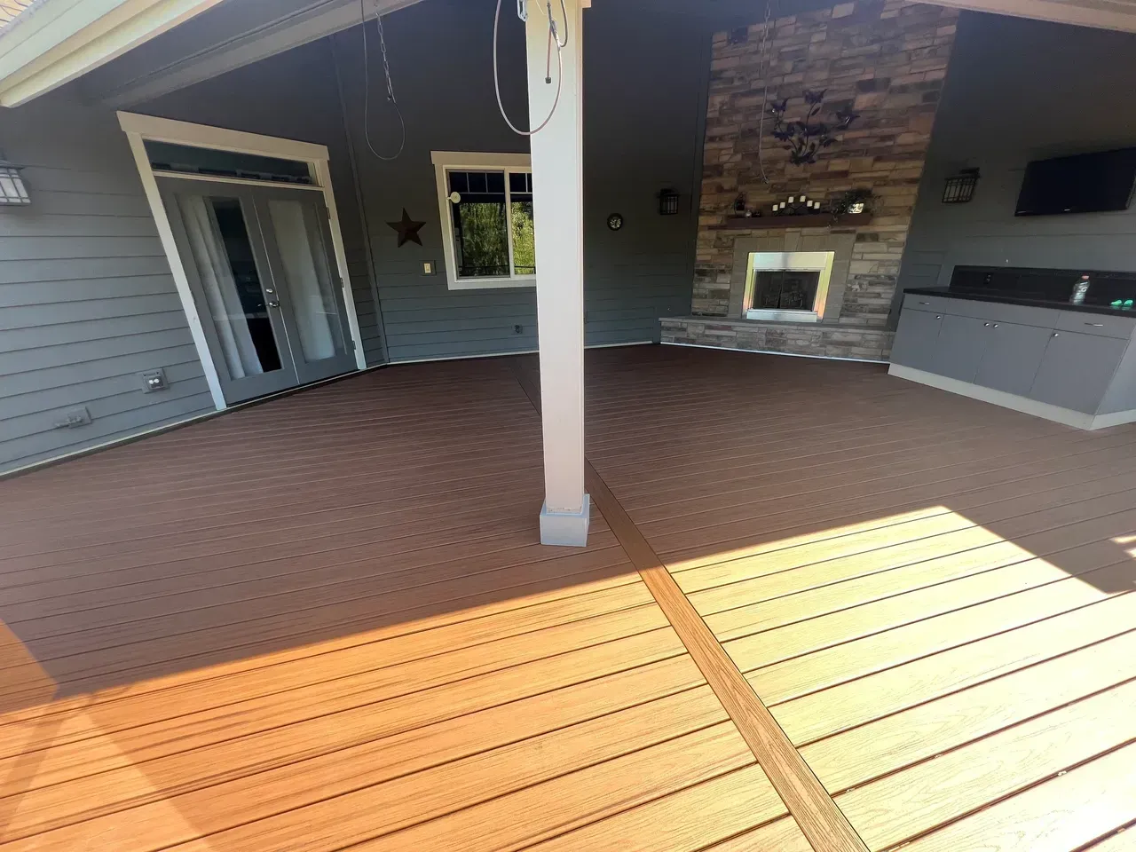 Brown composite deck with a covered outdoor living area featuring a fireplace and built-in grill.