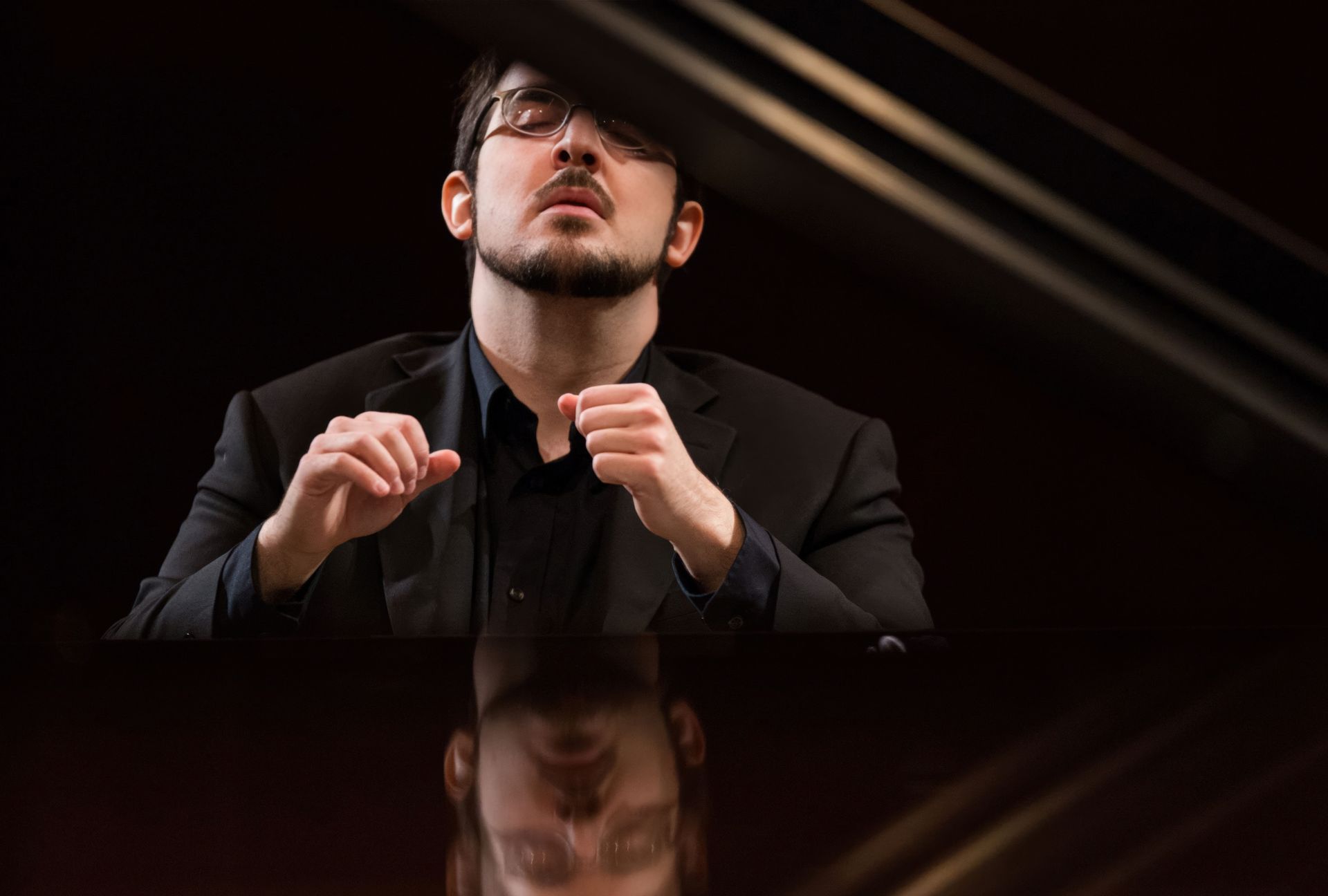 A man in a suit and glasses is playing a piano.