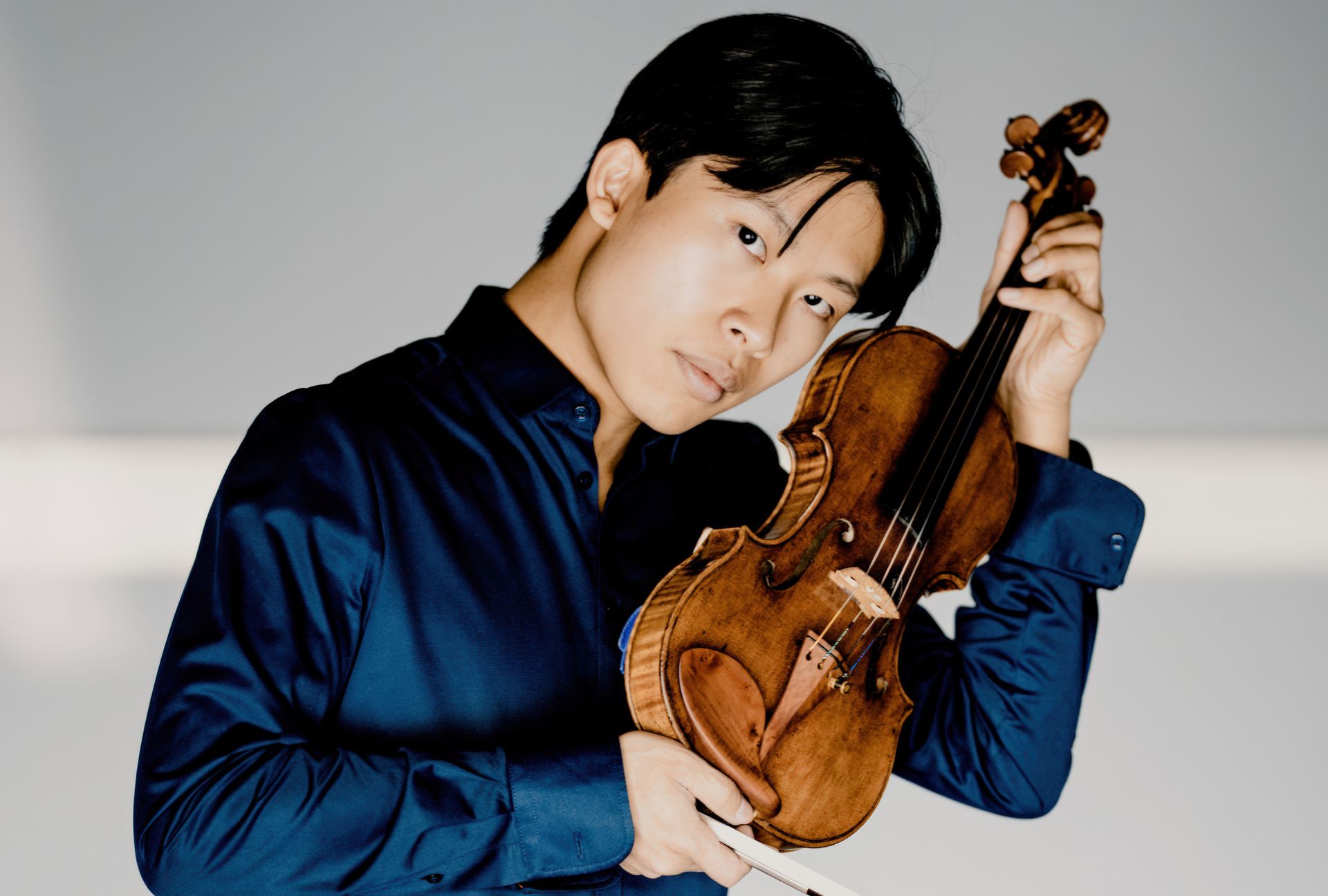 A young man in a blue shirt is holding a violin.