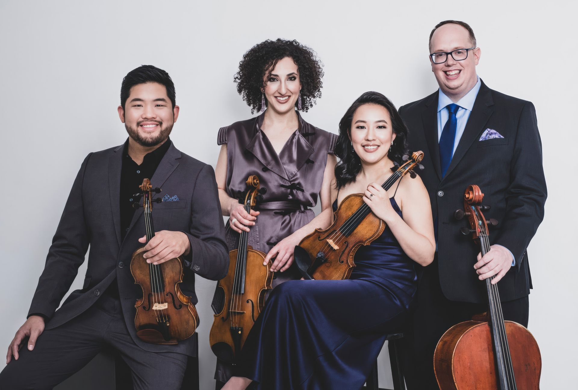 A group of people standing next to each other holding violins and cello.