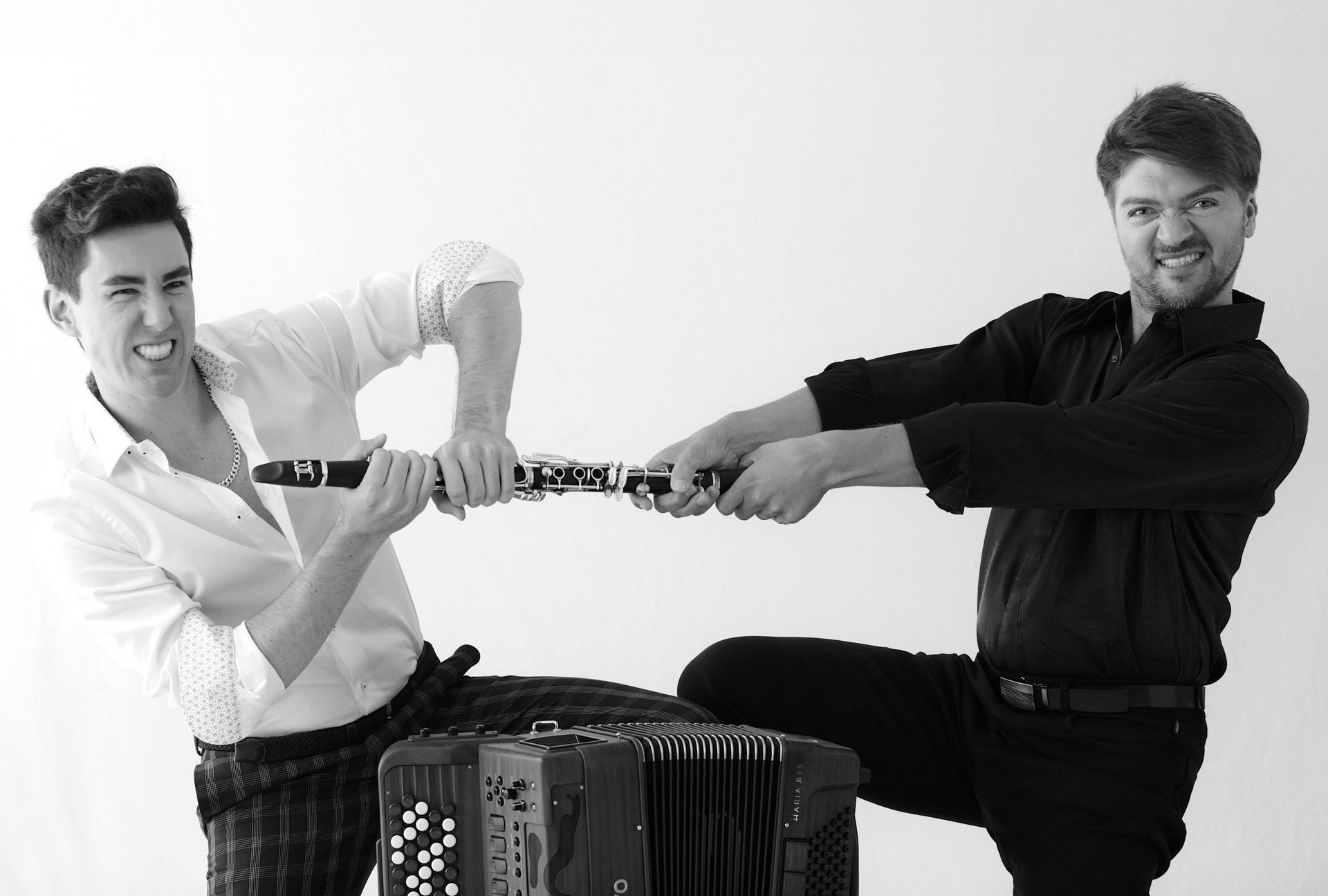 Two men are jokingly fighting over a clarinet with an accordion in the forefront.